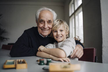 Portrait of happy watchmaker and his grandson sitting at table - GUSF02180