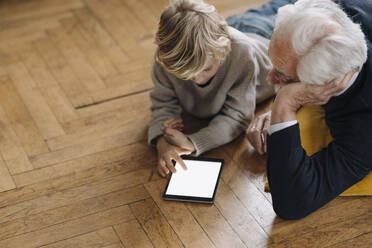 Großvater und Enkel liegen zu Hause auf dem Boden und benutzen ein Tablet - GUSF02182