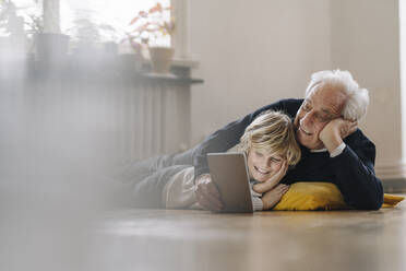 Glücklicher Großvater und Enkel, die zu Hause auf dem Boden liegen und ein Tablet benutzen - GUSF02183