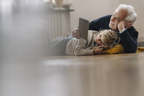Großvater und Enkel liegen zu Hause auf dem Boden und benutzen ein Tablet - GUSF02184