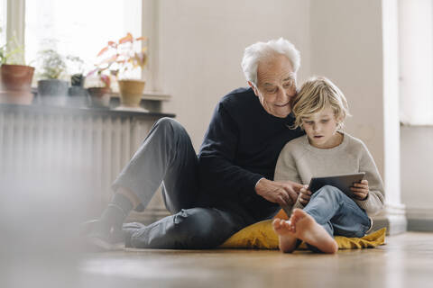 Großvater und Enkel sitzen zu Hause auf dem Boden und benutzen ein Tablet, lizenzfreies Stockfoto