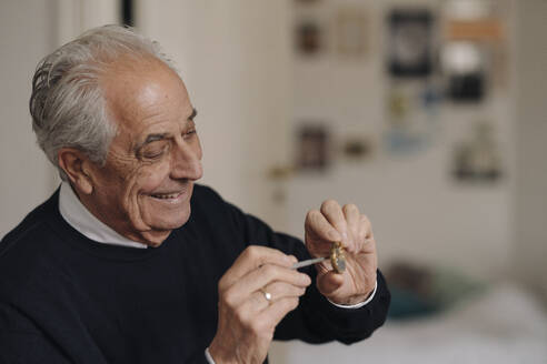 Lächelnder älterer Mann, der zu Hause eine Uhr repariert - GUSF02190