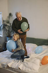 Glücklicher Großvater und Enkel spielen mit Luftballons auf dem Bett zu Hause - GUSF02207