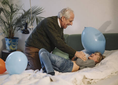 Happy grandfather playing with grandson on bed at home - GUSF02208