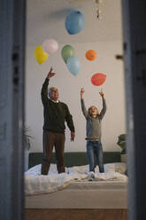 Glücklicher Großvater und Enkel spielen mit Luftballons auf dem Bett zu Hause - GUSF02209