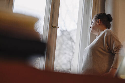 Ernste ältere Frau schaut zu Hause aus dem Fenster - GUSF02217