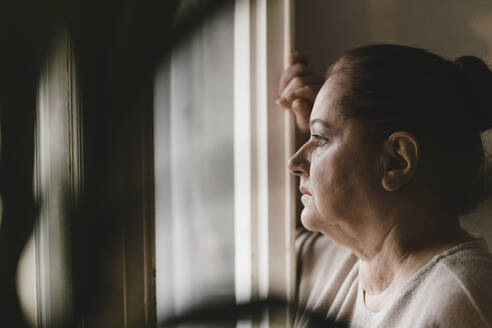 Serious senior woman looking out of window at home - GUSF02222