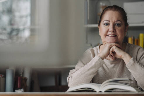 Porträt einer lächelnden älteren Frau mit Buch zu Hause - GUSF02230