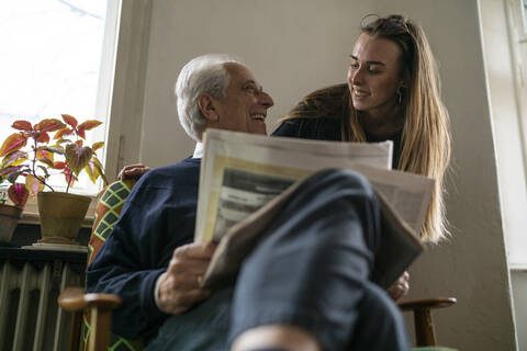 Happy young woman and senior man with newspaper at home stock photo