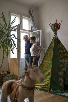 Älteres Paar steht im Kinderzimmer und schaut aus dem Fenster - GUSF02258