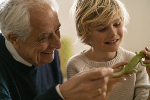 Glücklicher Großvater und Enkel spielen mit einem Spielzeugchamäleon, lizenzfreies Stockfoto