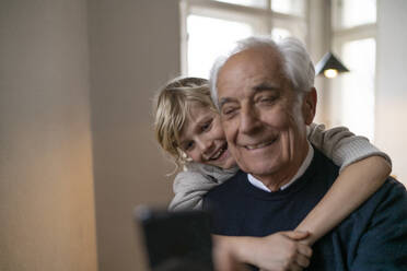 Glücklicher Enkel umarmt Großvater mit Handy zu Hause - GUSF02267