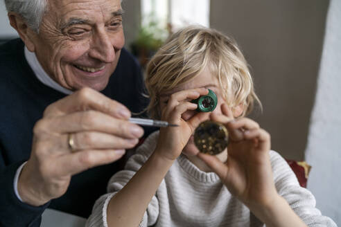 Watchmaker and his grandson examining watch together - GUSF02275