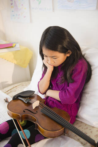 Schmollendes vietnamesisches Mädchen mit Geige im Schlafzimmer, lizenzfreies Stockfoto