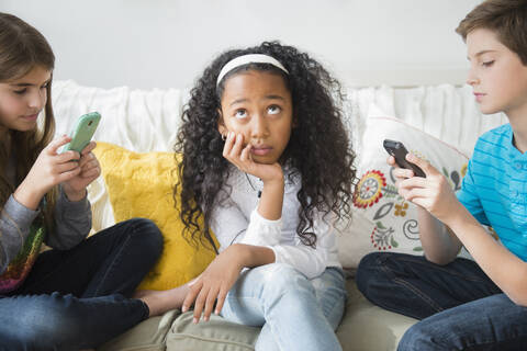 Genervtes Mädchen ignoriert Freunde, die auf dem Sofa Handys benutzen, lizenzfreies Stockfoto