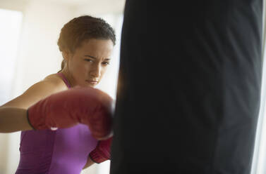 Mixed race woman hitting punching bag in gym - BLEF10415