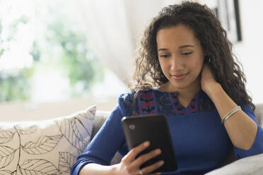 Gemischtrassige Frau benutzt digitales Tablet auf dem Sofa - BLEF10419