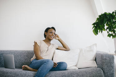 Smiling woman sitting on couch at home with laptop - SODF00030