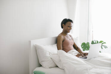 Lächelnde Frau, die zu Hause im Bett liegt und einen Laptop benutzt - SODF00033