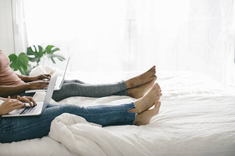 Legs of two women lying in bed at home using laptops stock photo