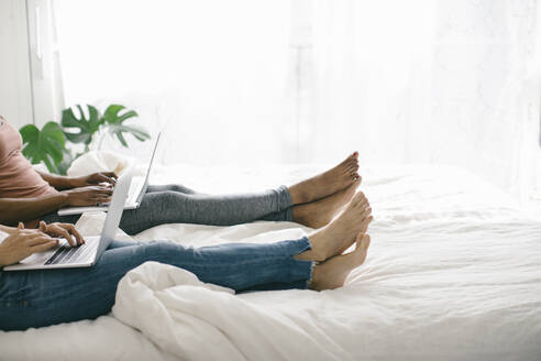 Beine von zwei Frauen, die zu Hause im Bett liegen und Laptops benutzen - SODF00036