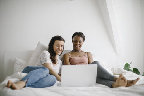 Zwei glückliche Frauen liegen zu Hause im Bett und schauen auf ihren Laptop - SODF00040