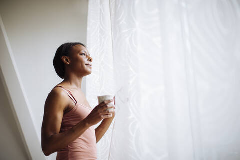 Frau zu Hause schaut aus dem Fenster, lizenzfreies Stockfoto