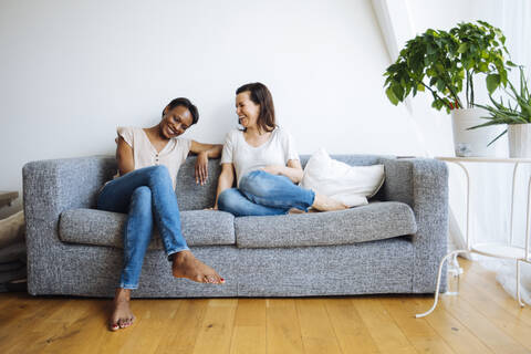 Zwei glückliche, entspannte Frauen sitzen zu Hause auf der Couch, lizenzfreies Stockfoto