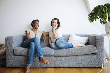 Two smiling women sitting on couch at home - SODF00053