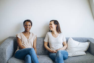 Zwei lächelnde Frauen sitzen zu Hause auf der Couch - SODF00054