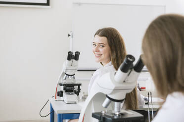 Junge Forscherin in weißem Kittel in einem naturwissenschaftlichen Kurs mit Blick zurück - AHSF00608