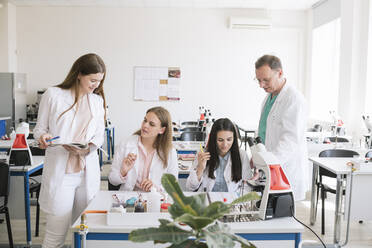 Students and teacher in white coats discussing in science class - AHSF00624