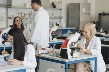 Ältere Forscherin im weißen Kittel bei der Arbeit im Labor, umgeben von anderen Forschern - AHSF00653