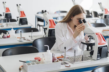 Junge Forscherin im weißen Kittel bei der Arbeit mit dem Mikroskop im Labor - AHSF00658