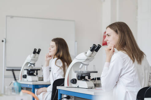 Blick von hinten auf junge Forscher in weißen Kitteln in einer wissenschaftlichen Klasse - AHSF00664