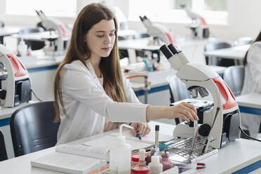 Young female researcher in white coat working in lab with a laboratory sample - AHSF00667