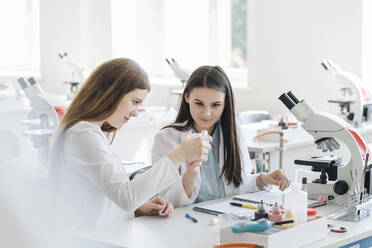 Young female researchers in white coats examining laboratory sample in science class - AHSF00672