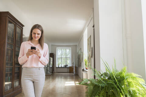 Junge Frau benutzt Smartphone im Flur, lizenzfreies Stockfoto