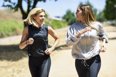 Mature woman running with her daughter in a park - JSMF01140