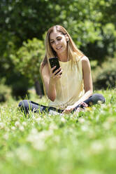 Frau benutzt ihr Smartphone und ruht sich nach dem Sport im Gras eines Parks aus - JSMF01146