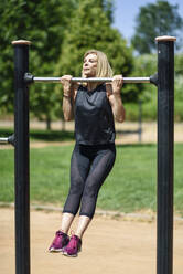 Mature woman exercising at a bar in a park - JSMF01153
