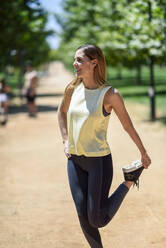 Smiling woman stretching leg on a path in a park - JSMF01166