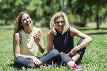 Happy sportive mature woman and her daughter sitting on a meadow in a park - JSMF01169