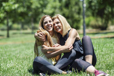 Sportliche reife Frau und ihre Tochter umarmen sich auf einer Wiese in einem Park - JSMF01170