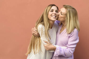 Happy mature woman hugging and kissing her daughter at a red wall - JSMF01176