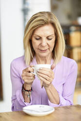 Mature woman drinking coffee sitting at an outdoor table in a cafe - JSMF01189