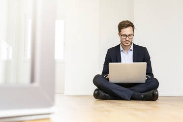 Businessman sitting on the floor using laptop - PESF01691