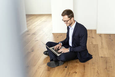 Smiling businessman sitting on the floor using laptop - PESF01695