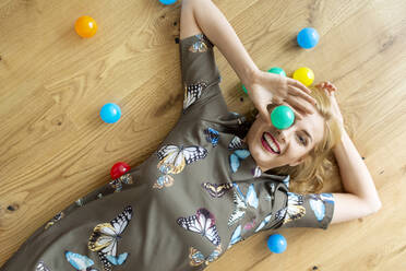 Laughing young woman lying on the floor with colourful balls - PESF01709