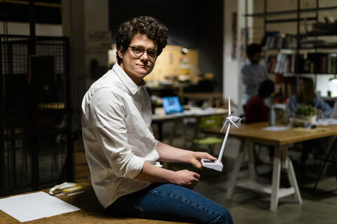 Porträt eines selbstbewussten Geschäftsmannes, der ein Windradmodell im Büro hält, lizenzfreies Stockfoto